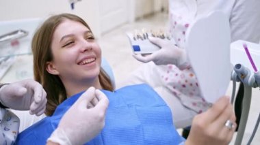 Dişçide gülümseyen kadın hasta. Stomatolog, klinikte güzel bir kadına diş rengini seçiyor. Diş beyazlatma şeması.