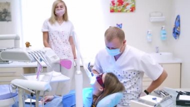 Diş konsepti. Profesyonel doktor stomatolojist iş başında. Dişçi, klinikte modern teknolojiyi kullanarak hastanın dişlerini tedavi ediyor..