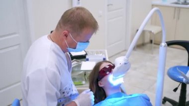 Dişçi kliniğinde modern ekipman. Kadın hasta diş hekimliğinde özel gözlüklerle tıbbi sandalyede yatıyor. Dişçi hastayı yeni teknolojiyle tedavi ediyor..