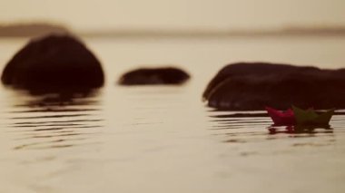 Kırmızı ve yeşil kâğıt gemiler nehirde. Origami Kağıt Tekneleri gölde yüzüyor. Güzel Dalgalar Dalgalanma Arkaplanı. Alışılmadık seyahat konsepti. Filtrelenmiş video.