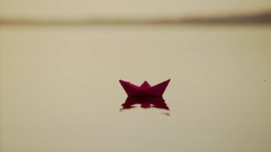 Nehirde Kırmızı Kağıt Gemi. Origami Kağıt Teknesi gölde yüzüyor. Güzel Dalgalar Dalgalanma Arkaplanı. Alışılmadık seyahat konsepti. Filtrelenmiş video.