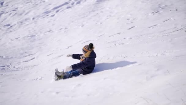 冬には小さな男の子が眠っていた 屋外の雪のスライドから幸せな子供が乗っています 冬のゲームや楽しみ スローモーション — ストック動画