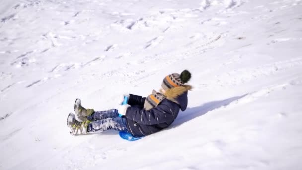 少年は丘の上で寝ていた 冬の公園での氷のスライド 雪の上のプラスチック板に乗って幸せな子供 — ストック動画