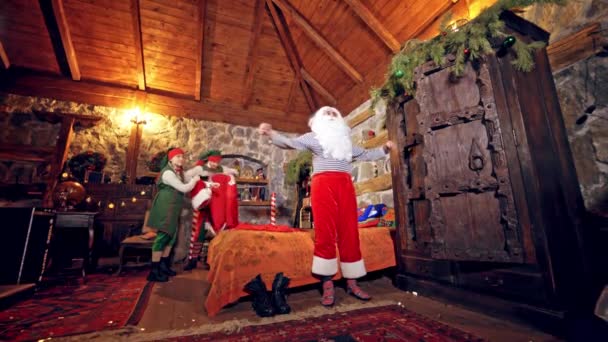 サンタクロースは朝起きる 2人のエルフはサンタが彼の家で赤い衣装を着るのを助ける クリスマス — ストック動画