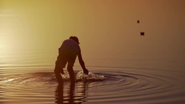 男孩在河里发射红绿相间的船 Origami纸船在孩子的手中美丽的波纹背景 旅行与自然的概念 日落时的录像 — 图库视频影像