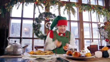 Erkek elf mandalinalarla oynuyor ve düşüyorlar. Özel dekore edilmiş bir odada kapüşonlu yeşil kostümlü bir elf. Yeni yıl ve Noel konsepti.