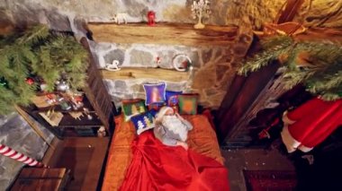Noel Baba yatağında özel dekore edilmiş bir odada uyuyor. O, elini yanağının altında tutuyor. Noel konsepti videoyu kapat. Noel ve yeni yıl yaklaşıyor. Hava görüntüsü. Yukarıdan video.