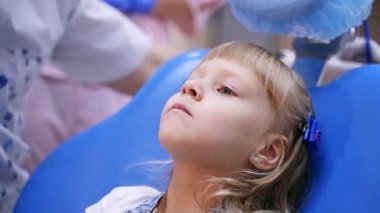 Stomatoloji sandalyesinde gülümseyen küçük bir çocuk. Çocuk hastaya oyuncak verilir. Sağlıklı diş konsepti - video kapat.