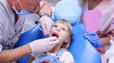 Stomatoloji bölümündeki küçük çocuk tedaviyi yeniden başlatıyor. Doktor dişçi aynası ile kızın dişlerini kontrol ediyor. Videoyu kapat..