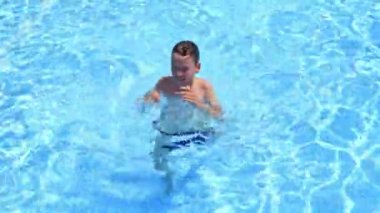 Mutlu çocuk dışarıda yüzüyor. Mavi yüzme havuzunun berrak sularında tatlı bir çocuk. Yazın su parkında neşeli vakit geçiren bir çocuk..