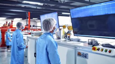 Teknisyenler robot ekipmanlarını kontrol ediyorlar. Koruyucu üniformalı profesyonel işçilerin arka planı modern fabrikanın içindeki büyük ekranlara bakıyor..