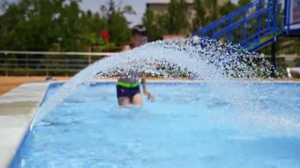 アクティブな少年はスイミングプールで楽しんでいます プールの屋外で小さな滝の近くで楽しい時間を過ごしている幸せな子供 幸せな夏 — ストック動画