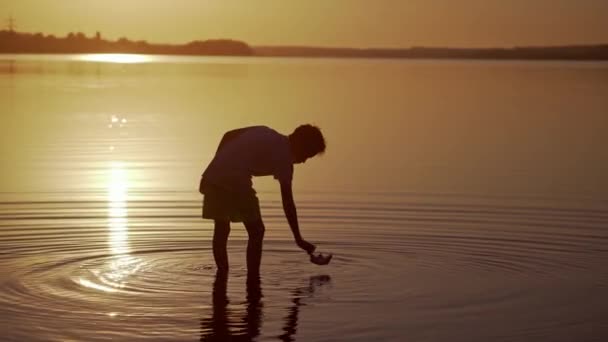 Fiú Közelében Naplementekor Silhouette Egy Fiú Vízben Papírhajóval Gyermek Üzembe — Stock videók