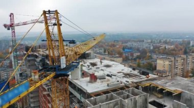 Şehirdeki inşaat alanının havadan görüntüsü. Büyük vinç ve çatıdaki işçiler. Yeni apartman inşaatı devam ediyor.