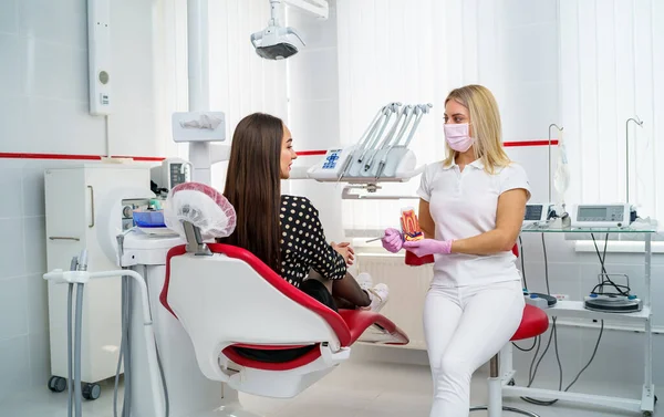 迷人的女牙医向坐在牙医椅子上的女病人展示了下巴的布局 专业牙医正在向一位女性病人解释治疗方法 — 图库照片
