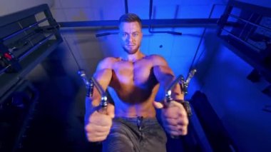 Güçlü vücutlu bir atlet spor salonunda egzersiz yapmaya çalışıyor. Aşağıdan bak. Mavi ışık filtresi. Kameraya bak..