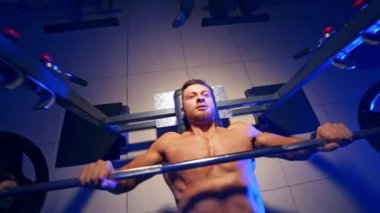 Vücut geliştirme eğitmeni beden eğitiminde ağırlık kaldırma egzersizi yapıyor. Yukarıdan bir video. Mavi ışık filtresi. Çıplak gövde. Güçlü kaslar.