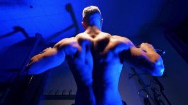 Kaslı adam çıtayı sıkıyor. Mavi arka planda spor salonunda egzersiz yapan güçlü bir adamın arka görünüşü. Yakın plan..