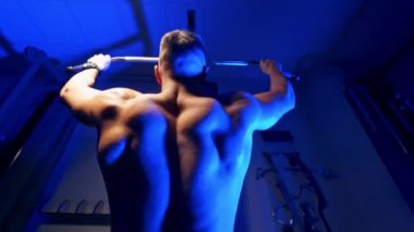 Egzersiz yapan bir sporcunun arka görünüşü. Sporcu spor merkezindeki bir simülatörde oturup egzersiz yapıyor. Mavi ışık.