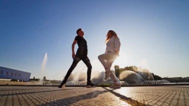 Dansçılar fıskiyeye karşı. Genç çift şehir arka planında modern bir dans sergiliyor. Günümüz gençlerinin serbest stil dansı güneşin sızıntıları arasında..