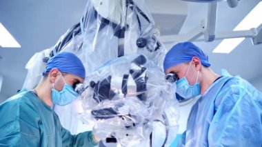 Uzmanlar mikroskoba bakıyor. Ameliyatı tıp üniformalı cerrahlar yapar ve klinikte modern ekipmanlar kullanır. Tıpta yeni teknolojiler.