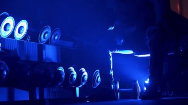 Spor salonunda spor yapan atletik bir adam. Halterlerle egzersiz yapıyor. Güçlü erkek, çıplak karın kasları var. Mavi koyu ışık filtresi. Seçici odak.