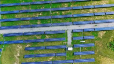 Mavi panelleri olan modern güneş istasyonu, parlak bir güneş ışığı altında yeşil çimlerle birlikte sahada duruyor. Yeşil enerji konsepti. Alternatif güç. Hava görünümü.