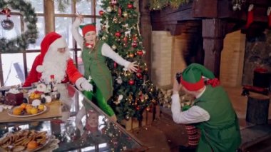 Noel Baba ve elf Noel ağacının yanında. Komik elf, Noel süslemeli odada peri karakterlerinin fotoğrafını çekiyor..