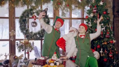 Peri periler Noel Baba 'yla fotoğraf çekiyor. Beyaz sakallı Noel Baba ve yeşil kostümlü elfler Noel tatilinde selfie çekiyorlar. Noel süslemeleri.