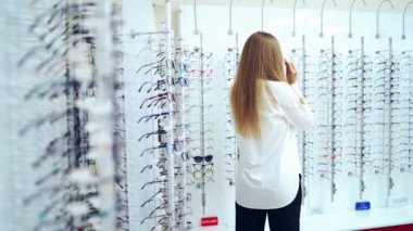 Optik mağaza. Kapalı alanda gözlük seçen bir kadın. Beyaz bluzlu genç bir kız yeni gözlük deniyor. Şık gözlükler takıyor. Görme konsepti.