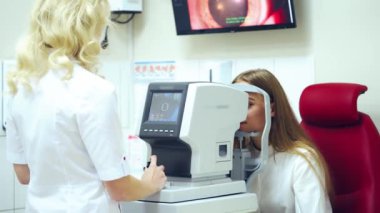 Doktor modern cihazda hastanın gözlerini inceliyor. Göz doktoru klinikte refraktometresi olan genç bir kadının görüşünü kontrol ediyor..