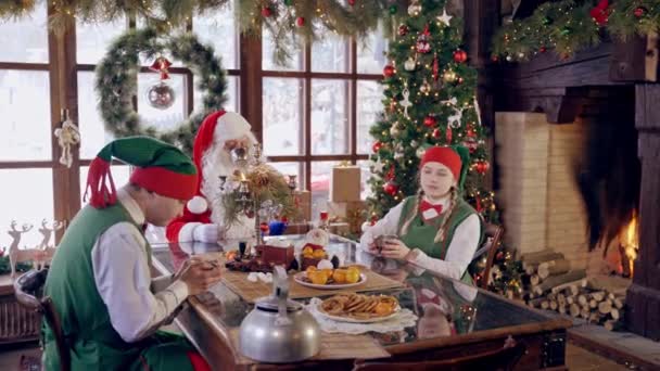 Télapó Manókkal Vidám Manók Ülnek Asztalnál Mikulással Teáznak Karácsonyi Háttérben — Stock videók