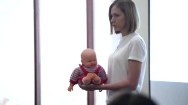 Halka açık bir toplantıda oyuncak bebeği olan genç bir kadın. Kadın öğretim üyesi elinde bir bebekle konuşma yapıyor ve küçük çocuklara nasıl bakılacağını anlatıyor..