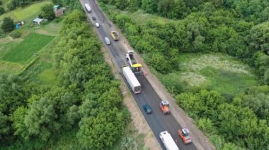 Otoyoldaki yol çalışması. Yaz mevsiminde yol şantiyesinin yakınından geçen kamyonlar ve arabalar. Hava görüntüsü. Kamera yukarıdan aşağıya hareket eder.