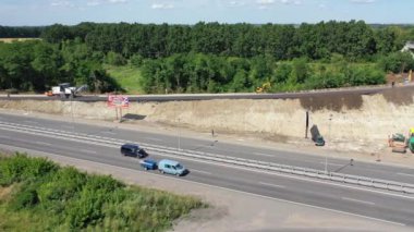 Otobanda arabalar ve kamyonlar. Yeni yol inşaatı. Yeni asfalt yol döşeyen ağır makineler. Güneşli bir yaz gününde otoyolun yakınında bitmemiş bir yol. Üst görünüm.