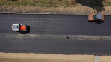 Ağır makineler yeni asfaltı düzleştiriyor. Yazın otoyolda çalışan yol silindirleri. Yeni yol inşaatı. Yukarıdan bak. Hareket kamerası alttan üste.
