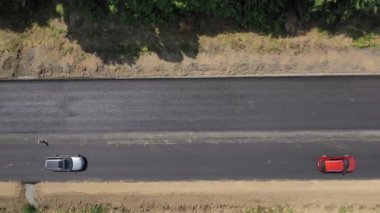 Yeni asfalt yolda giden arabaların üst görüntüsü. Yolun bitmiş kısmından yukarıdan görüntüle. Otomobiller otobanın bir tarafında sürüyorlar. Hava görünümü.