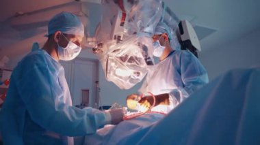 Beyin cerrahları mikroskopla ameliyat yapıyor. Ameliyathanede modern ekipman var. İki doktor ameliyat sırasında tıbbi aletler kullanıyor..