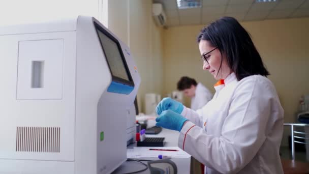 实验室里的血样专家在研究实验室现代机器上工作的身着医疗制服的女技术员 — 图库视频影像
