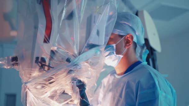 身穿医疗制服的医生对着现代显微镜看 戴口罩的外科医生通过显微镜进行手术 新医疗技术 — 图库视频影像