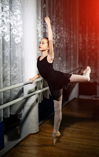 迷人的芭蕾舞演员 她的头发成束地伸展在窗边的腿上 穿着黑色服装 白色紧身衣的小女孩在芭蕾舞演播室接受训练 — 图库照片