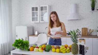 Modern mutfakta genç bir kadın. Güzel dişiler organik vitaminlerle dolu bir masada yemek yiyor. Sağlıklı bir yaşam tarzı. Diyet kavramı.