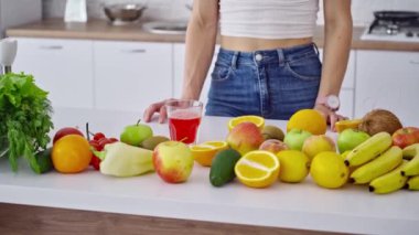 Organik meyveler masaya taze meyve suyu koyarlar. Kadının eli doğal vitaminlerin arka planında bir bardak taze meyve suyu alıyor. Sağlıklı yaşam tarzı.