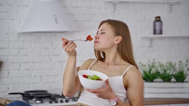 サラダを食べる若い女性 台所の背景に美しい女の子の嗅ぎや有機野菜を食べる 自然食の概念 — ストック動画