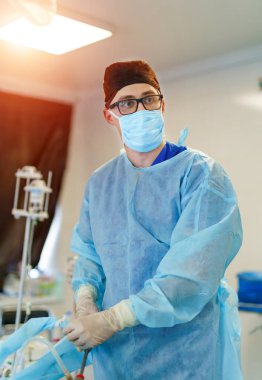 Ameliyathanede erkek cerrahın portresi. Modern hastane ameliyathanesinde önlüklü ve tıbbi maskeli bir doktor..