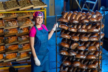 Fırında taze ekmekle rafların arkasında duran fırıncı bir kızın portresi. Sanayi ekmek üretimi