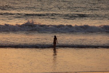 Gün batımında okyanusun yüksek dalgalarının arka planındaki kız.