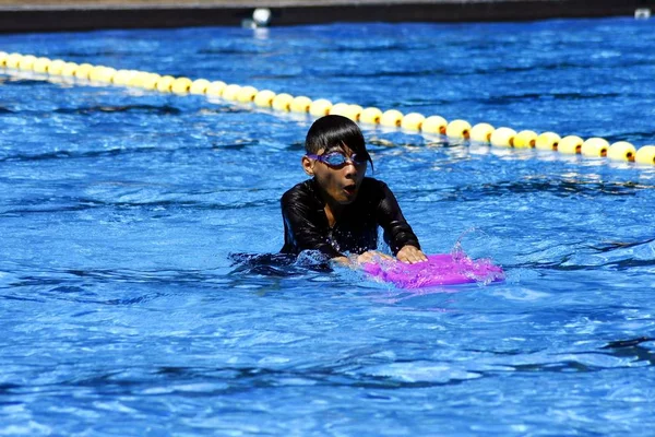 A kid learns how to swim in a pool with the help of a kickboard. — Stock Photo, Image