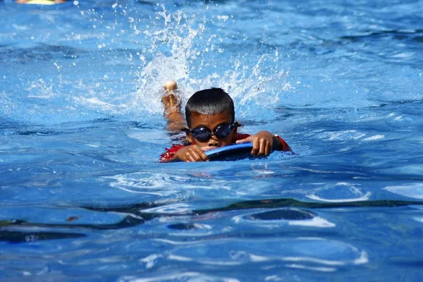 A kid learns how to swim in a pool with the help of a kickboard. — Stock Photo, Image