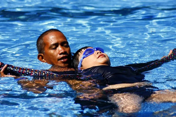 Genç bir çocuğun bir yüzme antrenör öğretir nasıl sırtında bir yüzme havuzunda yüzen. — Stok fotoğraf